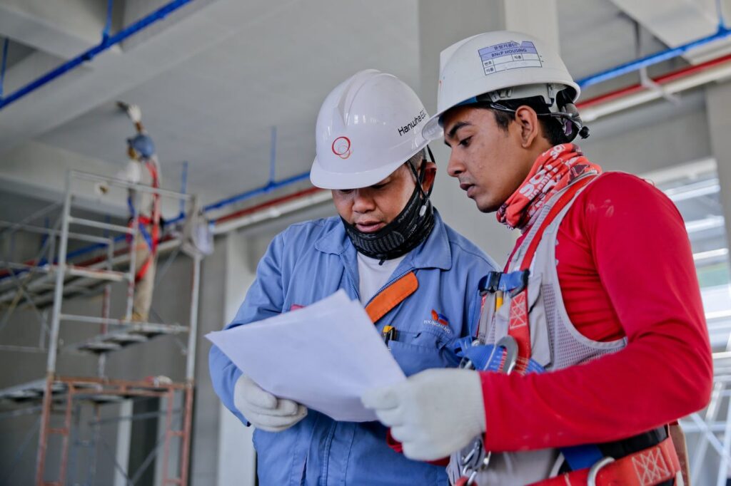Due tecnici con elmetto che leggono un documento in un ambiente di lavoro